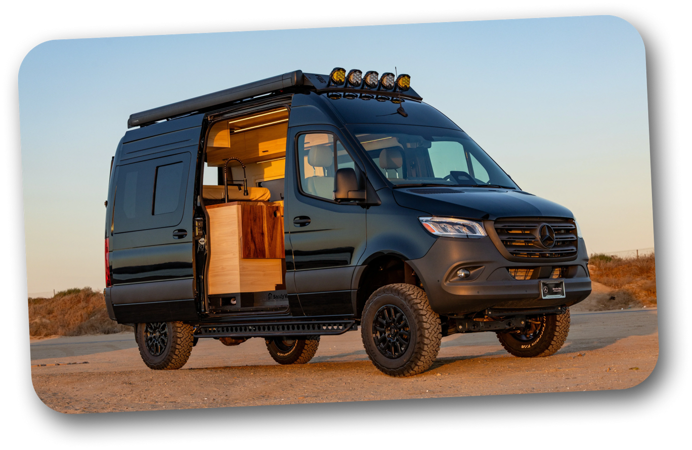A fully-loaded black Sandy Vans Sprinter camper van parked at sunset