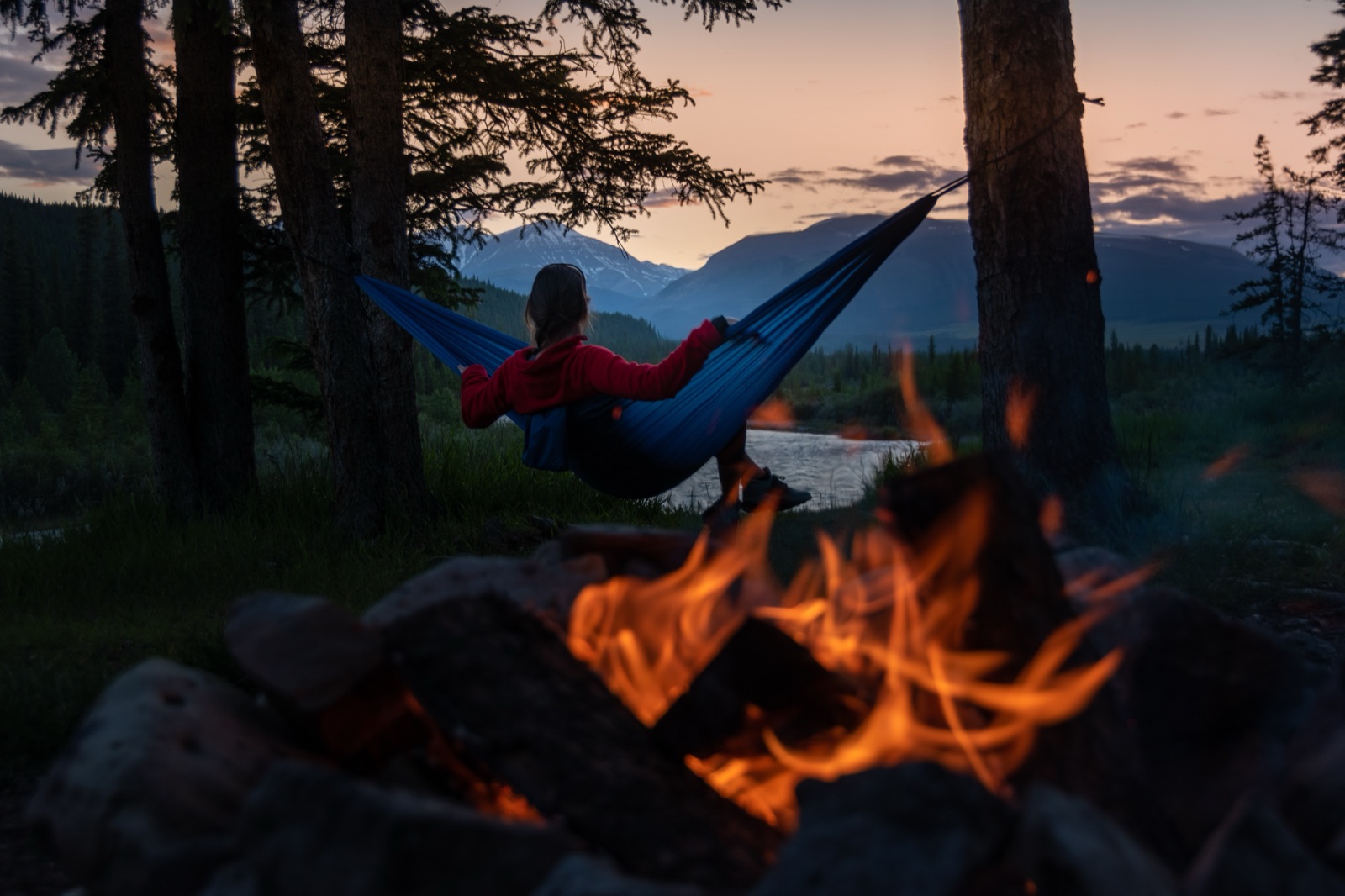 A camper relaxing in a hammock beside a campfire at dusk